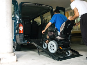 Man on wheelchair using accessible vehicle with ramp for transportation with driver helping