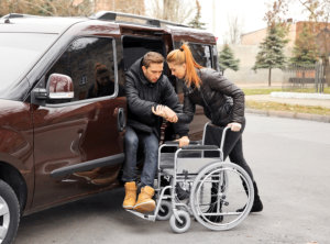 Young woman helping handicapped man to sit in wheelchair