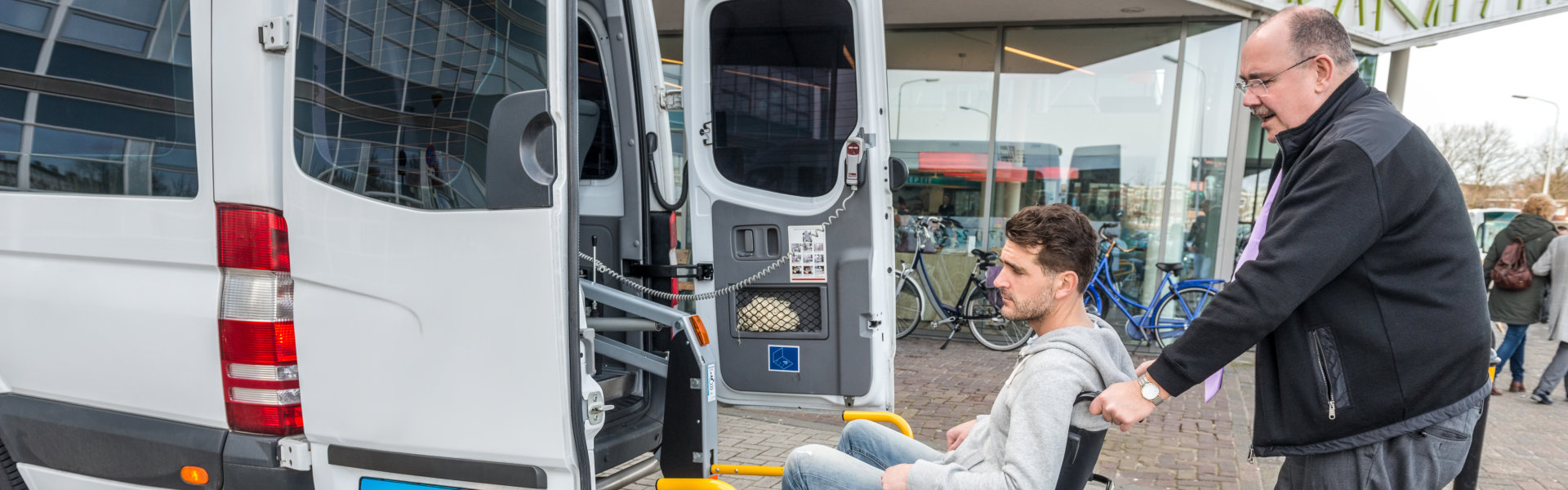 Taxi Driver Assisting Man On Wheelchair To Board Van