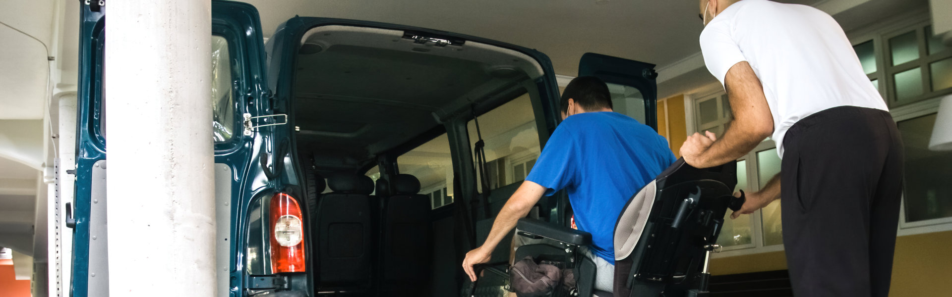 Man on wheelchair using accessible vehicle with ramp for transportation with driver helping